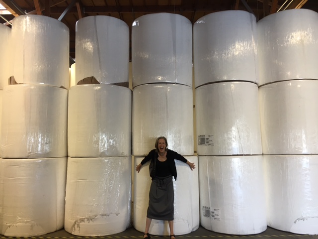 Mary Roach stands in front of giant paper rolls, smiling