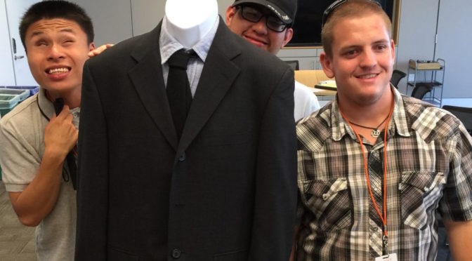 Youth stand next to mannequin wearing a suit and tie