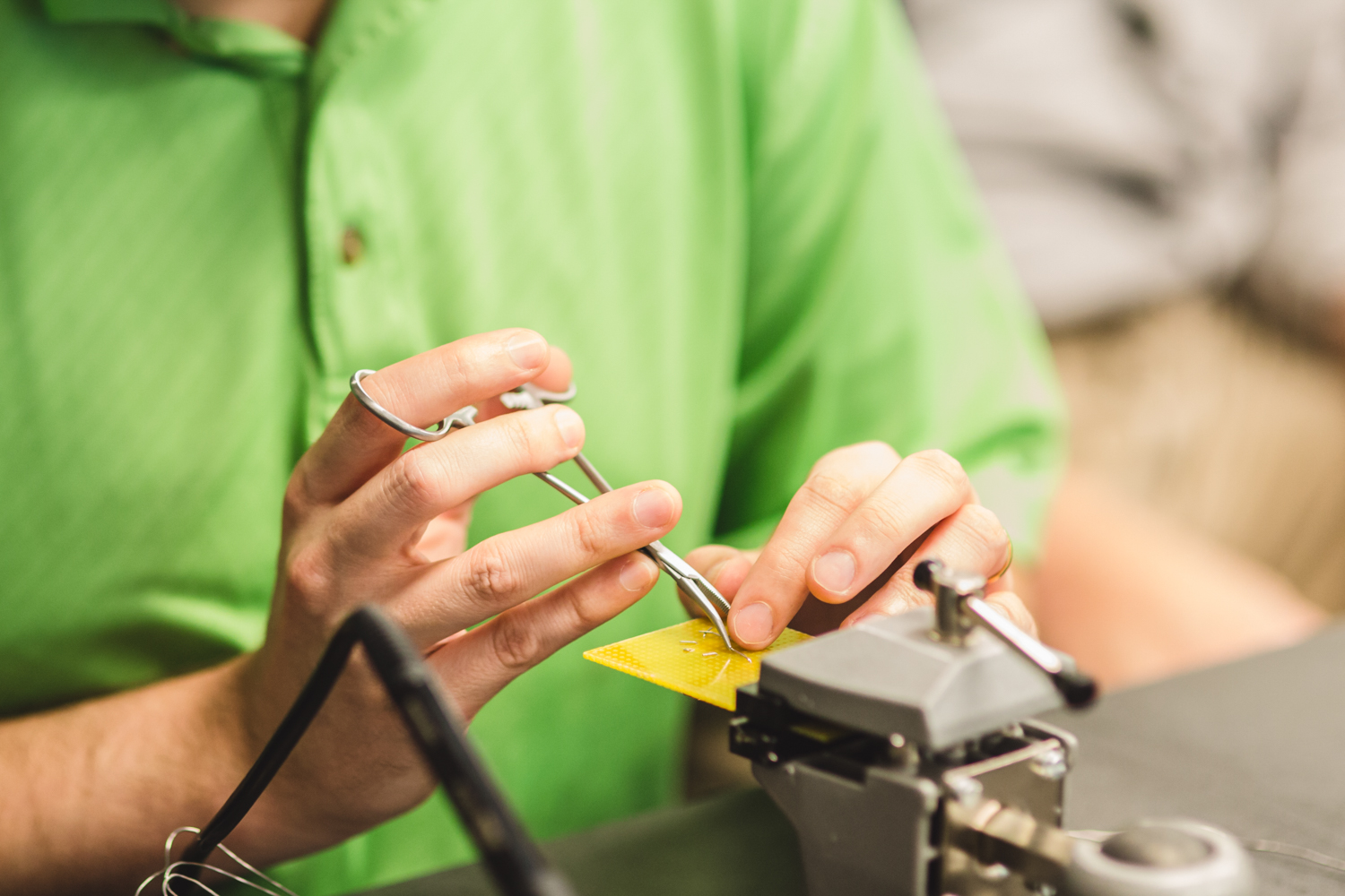 A student’s fingers slide down the length of a pair of stainless steel forceps to find the point of contact on the circuit board. This technique helps students who are blind create landmarks for soldering throughout the process. 