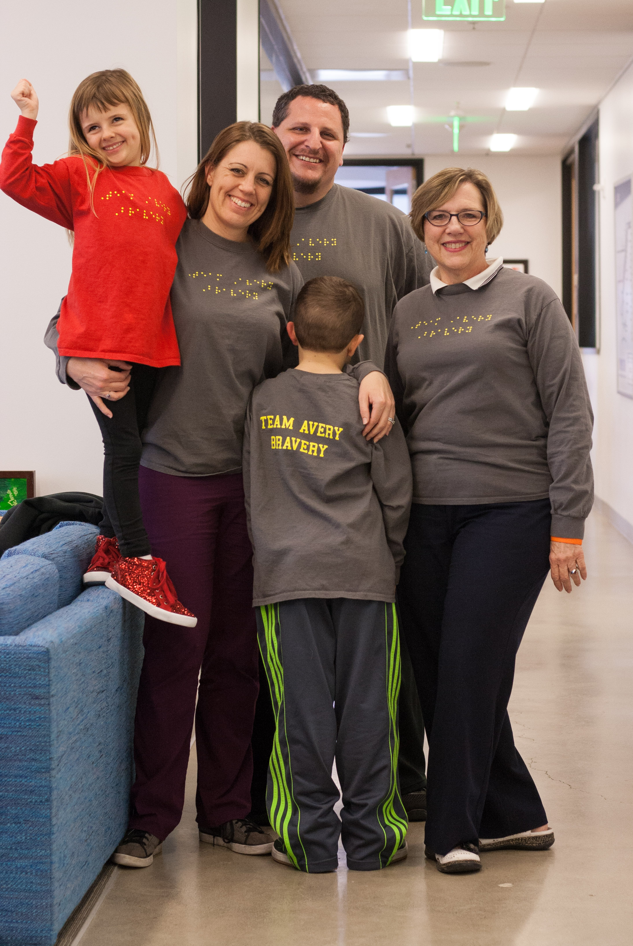Competitor Avery poses with her smiling family, who made shirts that say "Team Avery Bravery" in braille on the front and in text on the back.