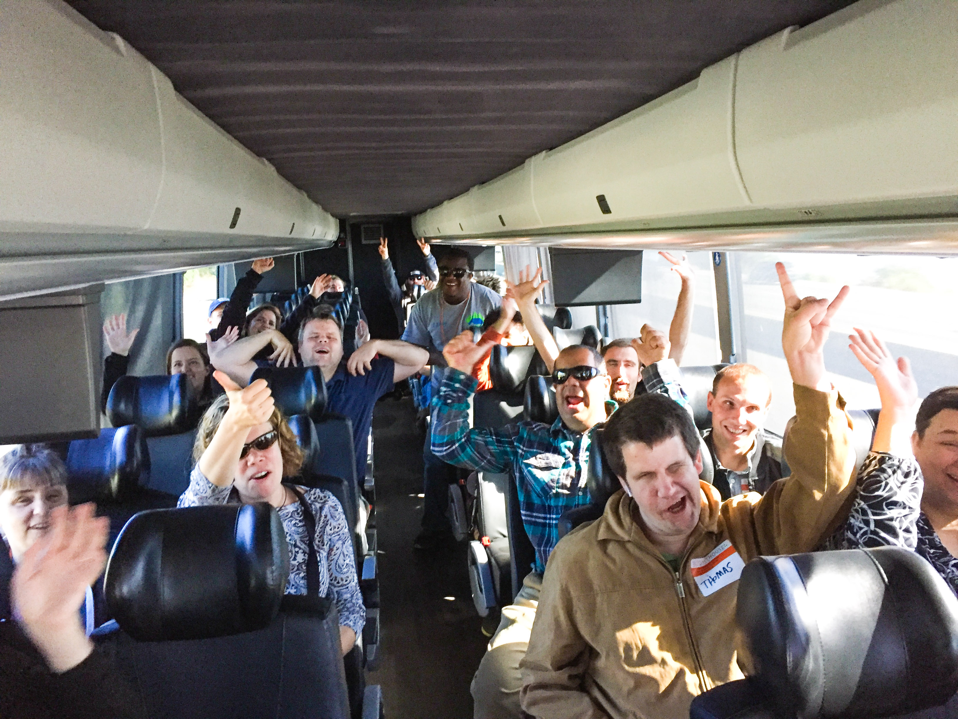 Participants in the bus on the way to Maker Faire raise their arms in celebration.
