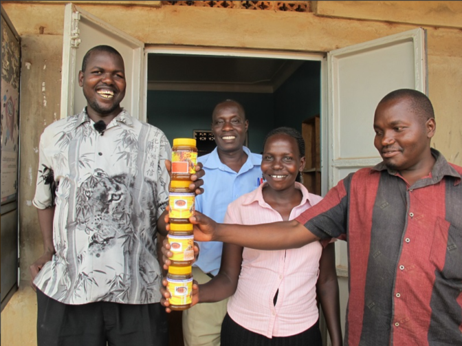 Ojok stands with a group of friends and fellow trainers, holding jars of Hive Uganda honey.