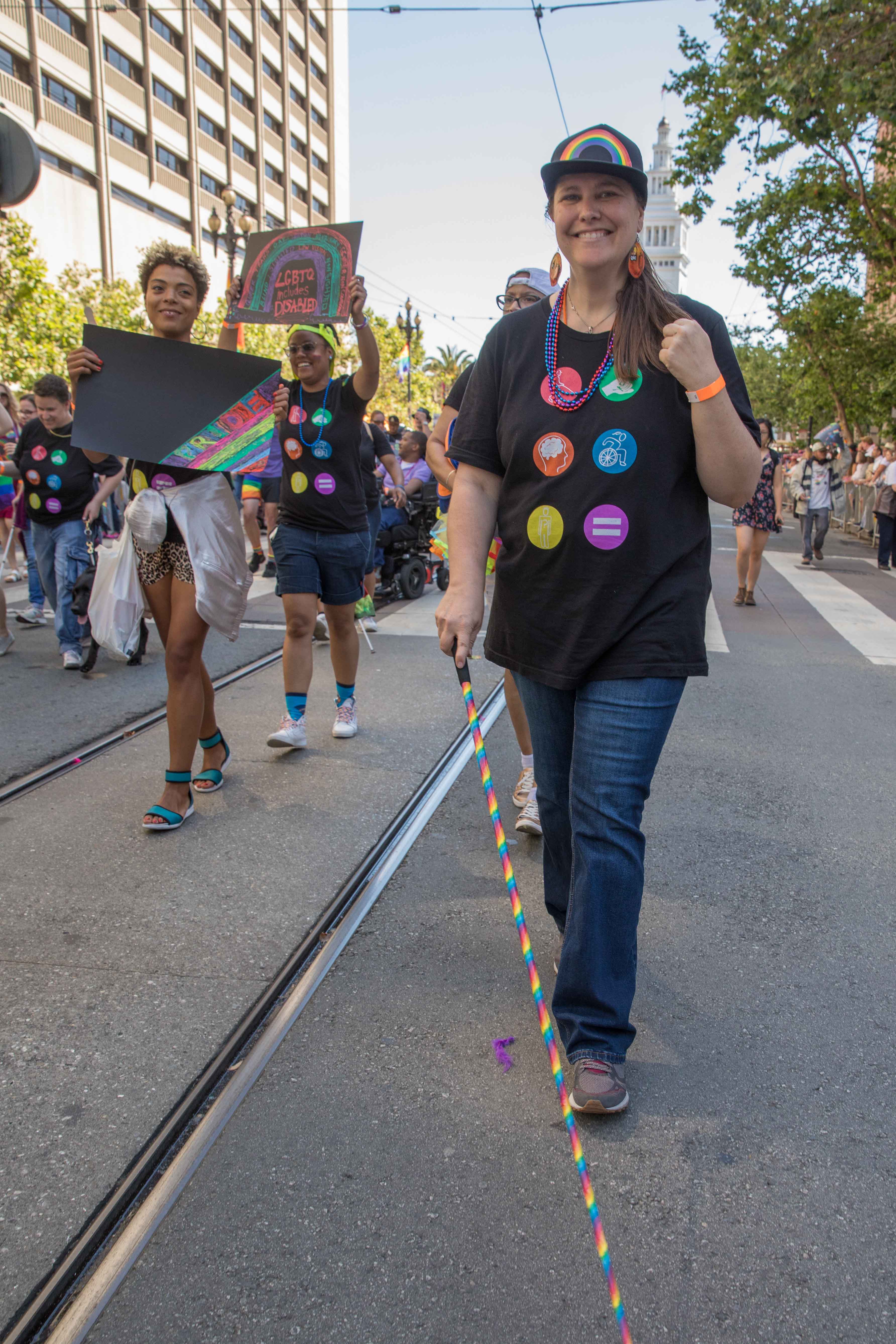 LightHouse Pride organizer Laura Millar smiles while marching, with her white cane wrapped in rainbow ribbon.