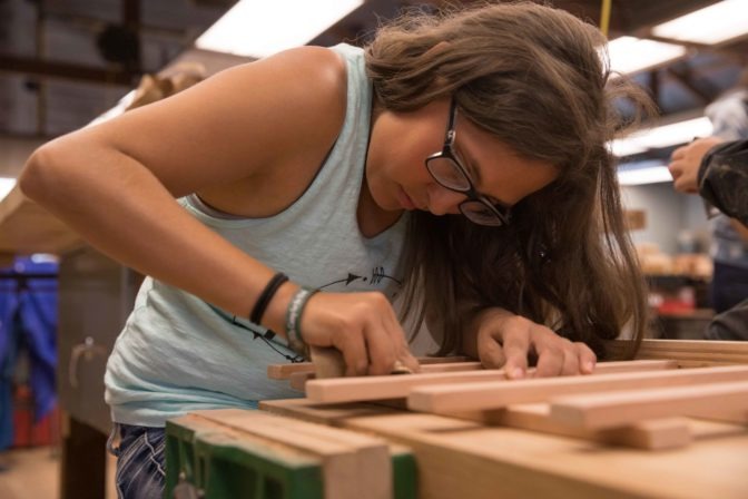 A female teen camper works on constructing and sanding a wooden music stand in the Art Barn.