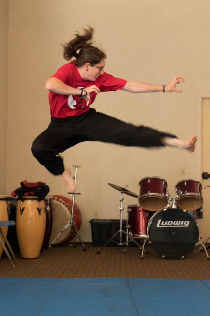 A camper jumps into the air and kicks to the side while practicing karate in the the Kiva.