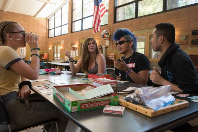 A group of teen campers play a lively game of Monopoly.