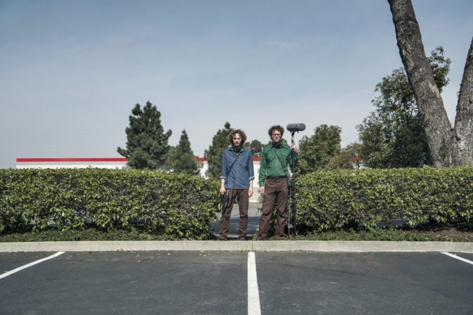 The World According to Sounds co-producers Chris Hoff and Sam Harnett stand in a parking lot with their recording equipment.