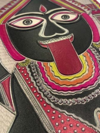 Closeup of a tactile version of The Hindu deity Kali, by Baua Devi, shows the deity's face in bright pinks, yellows and blacks with her tongue hanging out of her mouth.