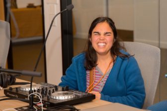 Audio Academy student Maycie sits grinning in front of her DJ equipment in the LightHouse board room.