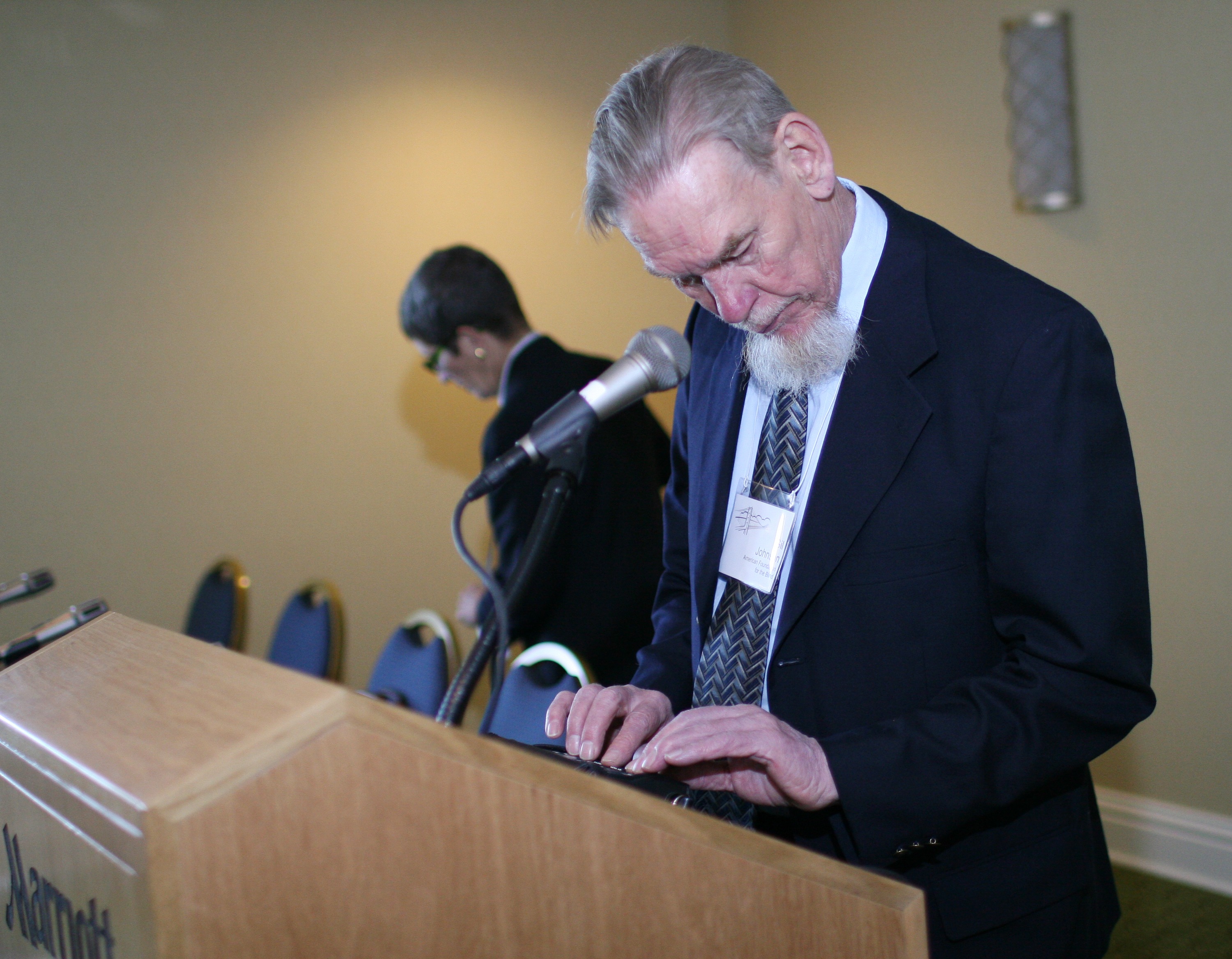 Gil Johnson speaks at a podium while reading from a braille display.