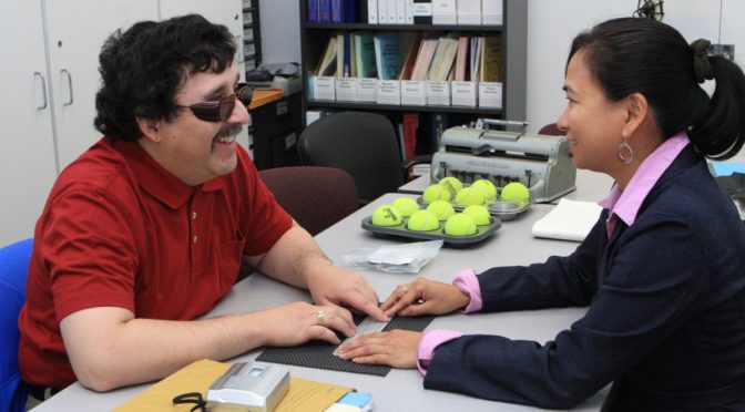 Braille instructor Divina shows student Ray a braille slate.