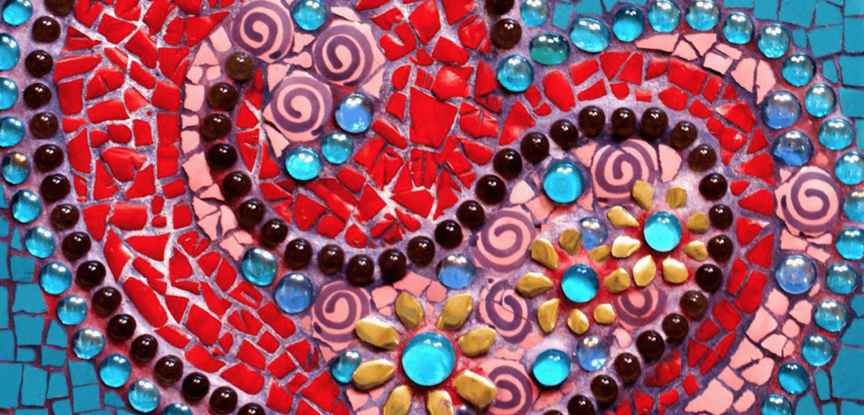 A swirl of pink, blue and orange glass beads flow through the center of a red, heart mosaic on a blue tiled background.