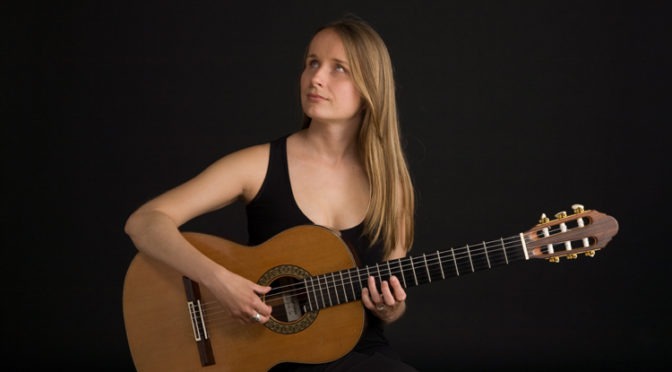 A portrait of Ioana Gandrabur, seated with her guitar.