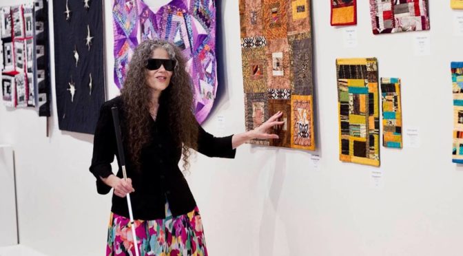 Claire Spector at the opening of her exhibit, "Blind Stitching", standing in front of her textiles.