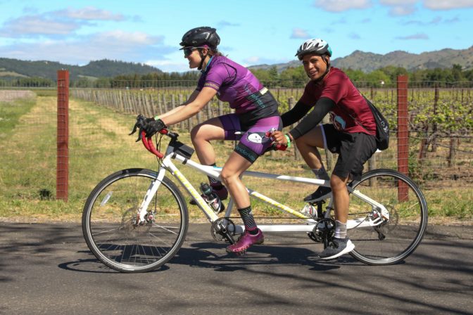 Tandem team Gabriella and Jeshua ride along a sun-dappled road in Napa.
