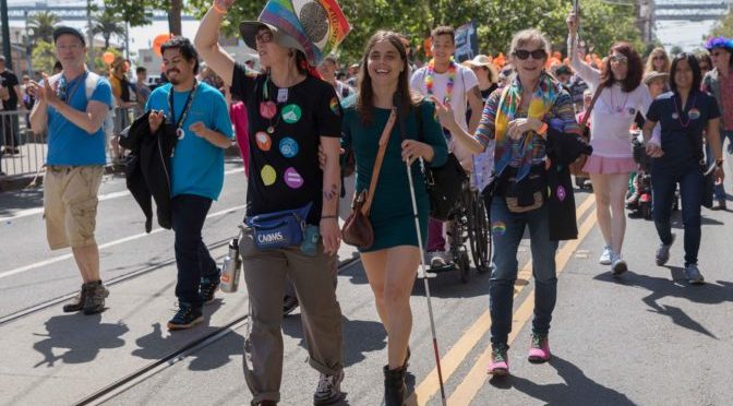 A pride participant with a cane walk side by side in the midst of our large Pride contingent.