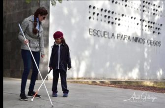 Conchita shows a little girl how to use a long white cane at a school in Mexico.]