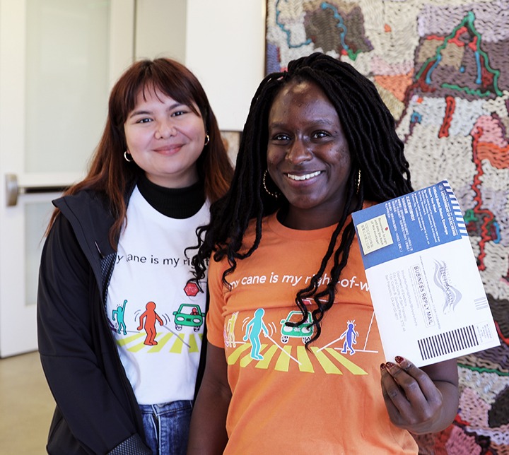 Blind voter Amber and LightHouse volunteer Aisha hold a sealed vote-by-mail ballot in 2019