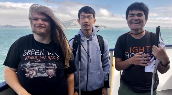 Tres estudiantes de la Academia Yes en un Ferry con sus bastones blancos, mirando a la cámara y sonriendo.
