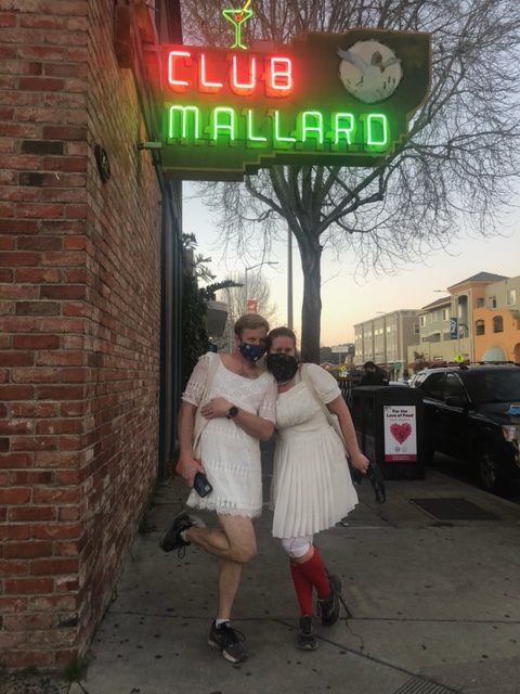 Two people wearing white dresses, masks and running shoes pose for a photo