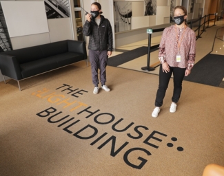 Two volunteers wearing LightHouse masks stand in the lobby of LightHouse headquarters. One holds a walkie-talkie.