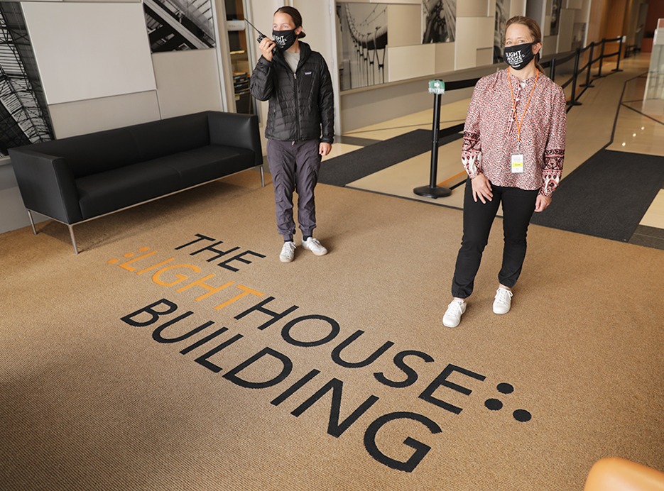 Two volunteers wearing LightHouse masks stand in the lobby of LightHouse headquarters. One holds a walkie-talkie.