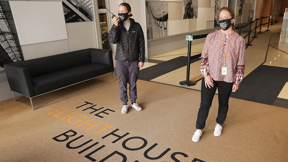 Two people wearing masks standing six feet apart in the LightHouse building lobby at 1155 Market Street