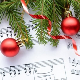 An image of sheet music, red ribbon, a red ornament, and pine tree branches