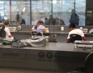 Three Perkins Braillers sit on a desk in focus in the foreground, three students working at three other Perkins Braillers are out of focus in the background