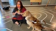 Maia Scott, wearing tie-dye, sits with her golden retriever guide dog