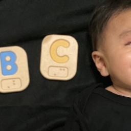 Little Learner is laying down next to ABC Braille blocks.