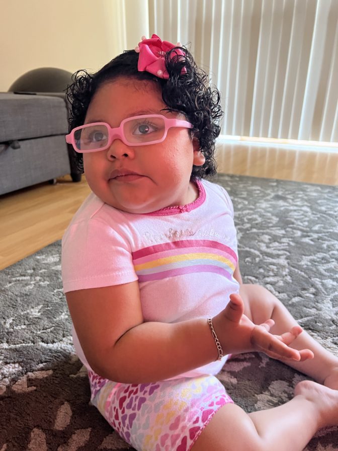 Little Learners girl wears glasses with a pink frame and a pink bow in her hair