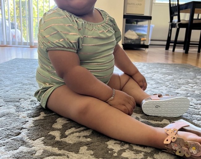 Little Learners girl sits on a rug on a hardwood floor and looks up, smiling
