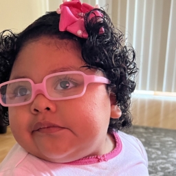 Little Learners girl wears glasses with a pink frame and a pink bow in her hair