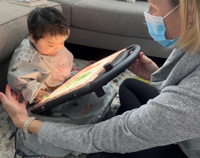 Maisara holds a lightboard with colorful tiles placed on it for her Little Learner to play