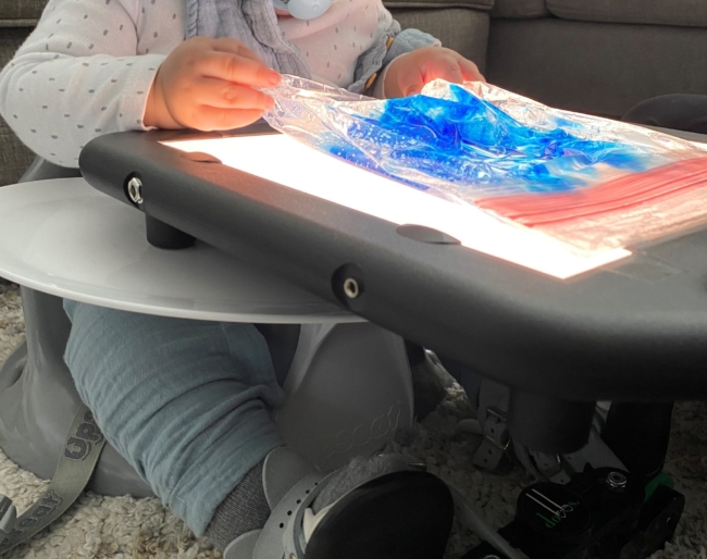 Little Learner with a pacifier in his mouth plays with a translucent blue material on a lightboard