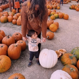 A mother holds both of her son’s hands as they stand in a pumpkin patch