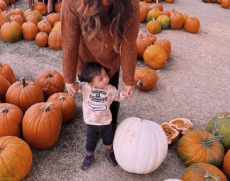 A mother holds both of her son’s hands as they stand in a pumpkin patch