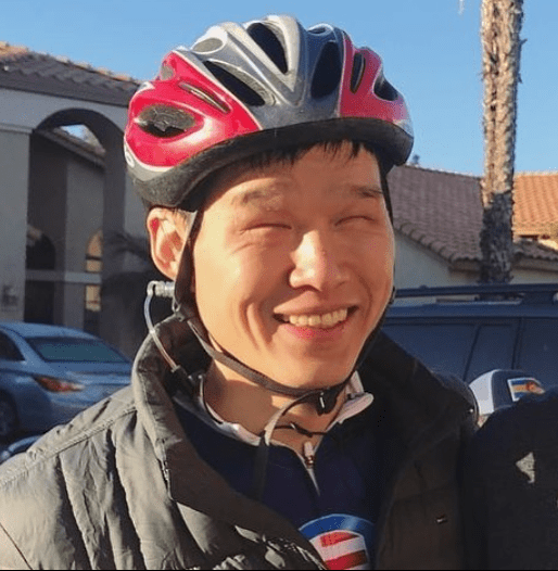 Jack Chen stands outdoors, wearing a helmet and athletic gear under a jacket