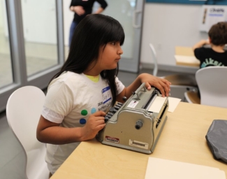 A child reads Braille on a sheet of paper inside a Perkins Brailler