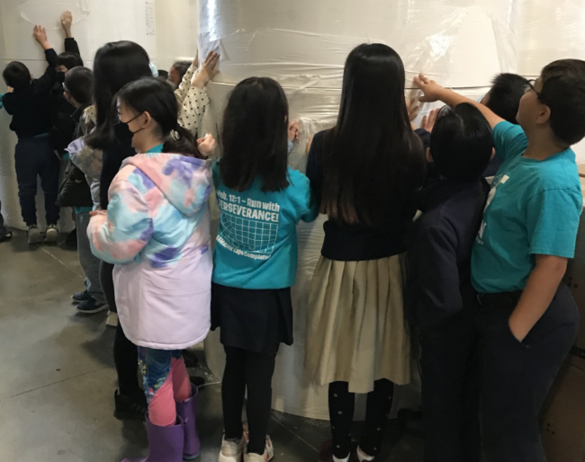 Students look at and touch a huge wrapped tissue roll