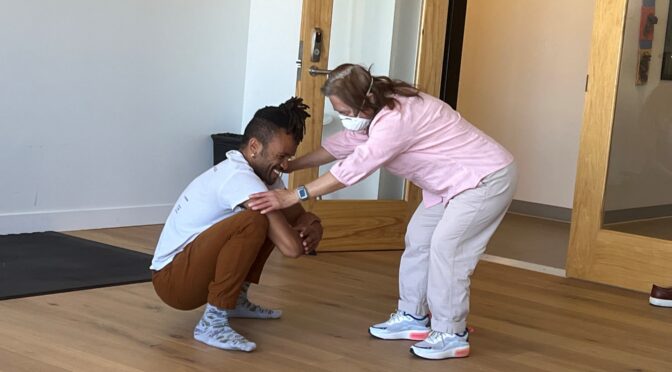 Gravity dancer, Gabrielle, Christian squats, and hold the hands of student Katlau, who bends over face-to-face and close up as they work together during and improvisational movement class.at LightHouse