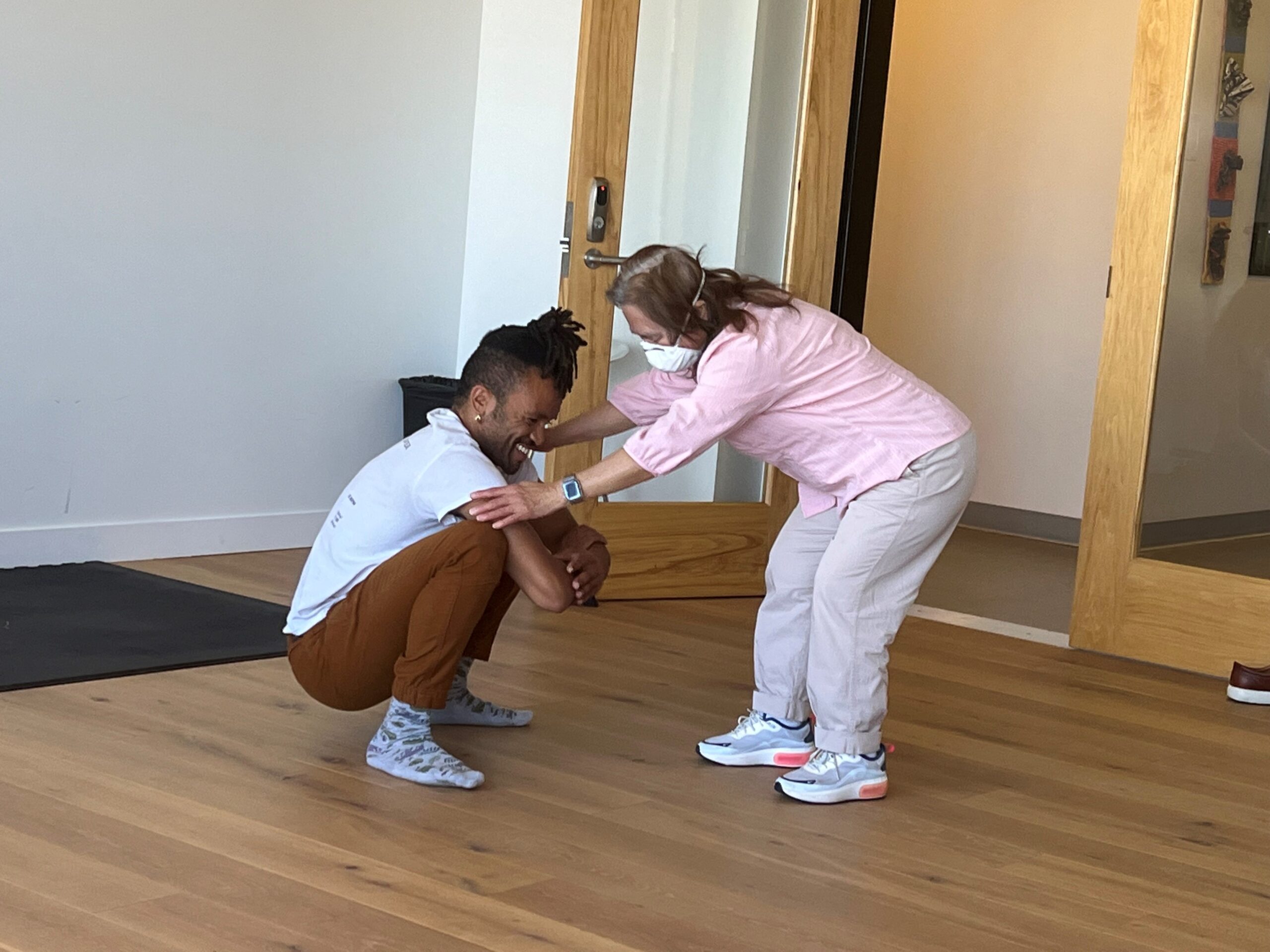 Gravity dancer, Gabrielle, Christian squats, and hold the hands of student Katlau, who bends over face-to-face and close up as they work together during and improvisational movement class.at LightHouse