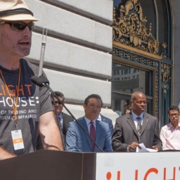 LightHouse Vice President of Programs, Scott Blanks, stands at a podium on the steps of San Francisco City Hall as officials and LightHouse students look on at a previous LightHouse Day