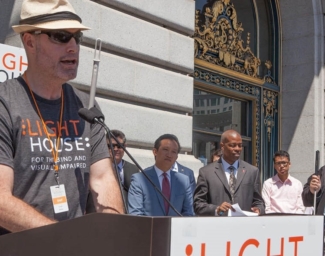 LightHouse Vice President of Programs, Scott Blanks, stands at a podium on the steps of San Francisco City Hall as officials and LightHouse students look on at a previous LightHouse Day