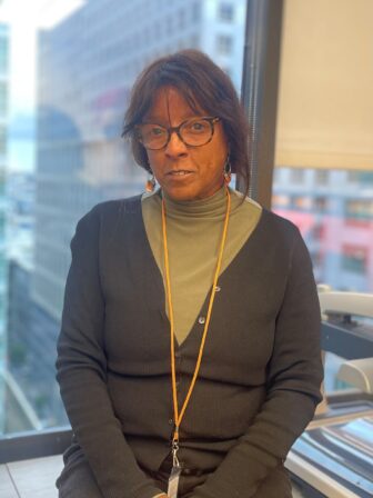 Sabrina Bolus, a black woman, wears an olive-green shirt under a dark gray sweater