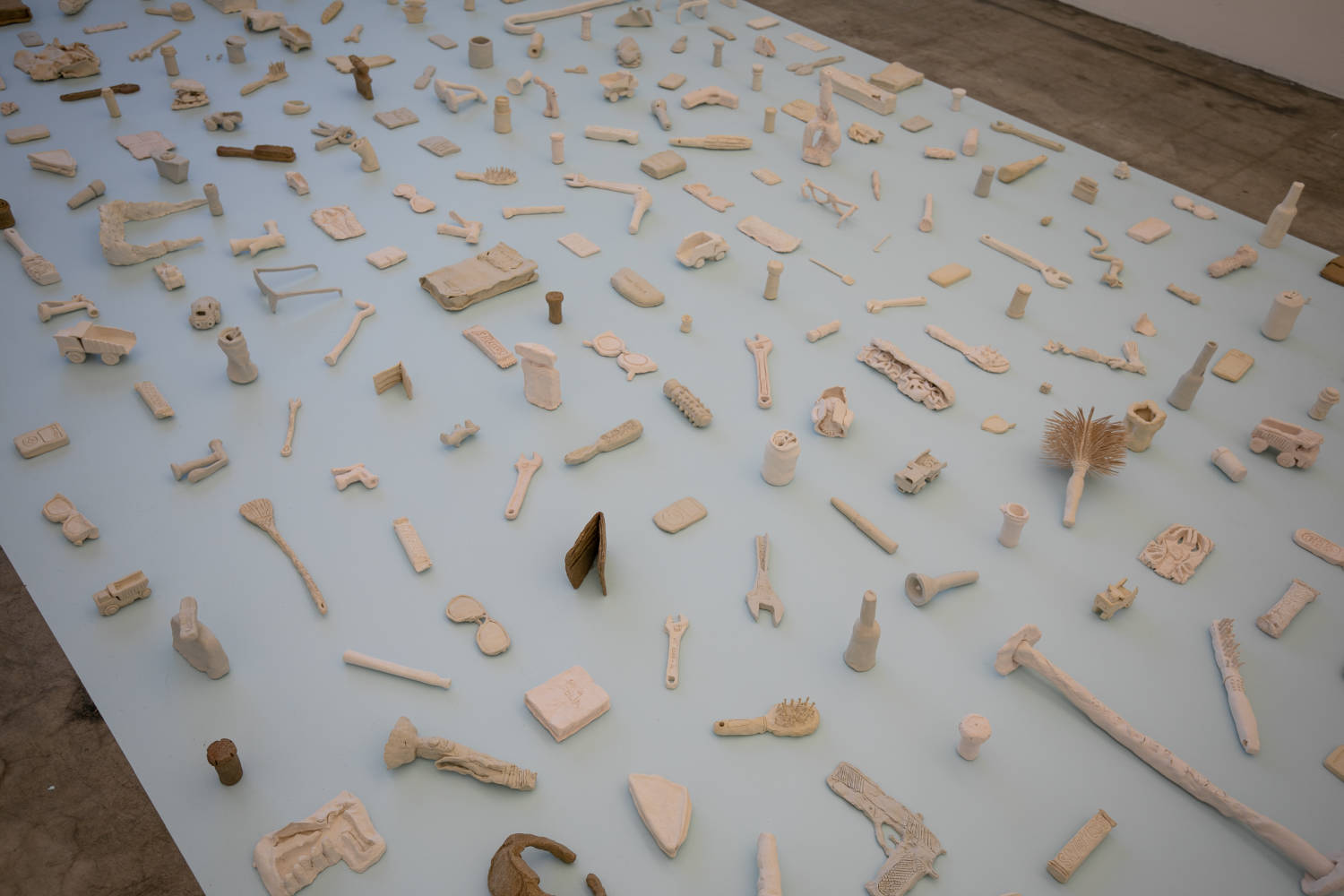 Clay replicas of everyday objects, made by Cara Levine, sit on a platform.
