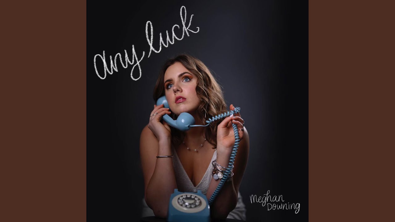 Meghan Downing’s cover art for her single “Any Luck”. She is looking up and off to the right side while holding the handle of a blue rotary phone.
