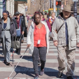 A group of people who are blind or have low vision using white canes walking in the crosswalk on Market Street in San Francisco