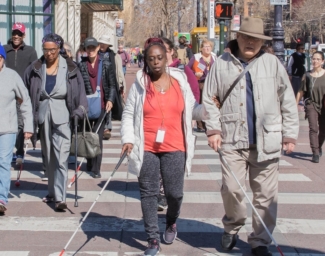 A group of people who are blind or have low vision using white canes walking in the crosswalk on Market Street in San Francisco